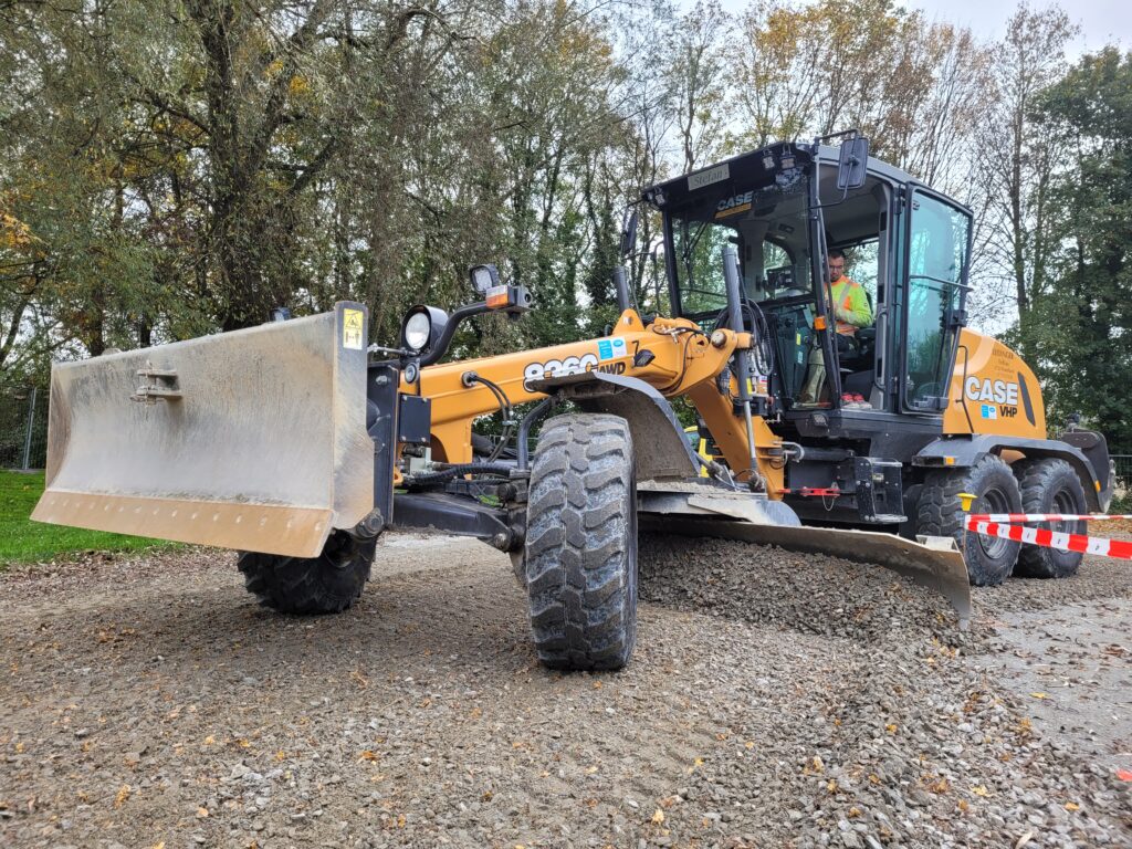 Eine große Baumaschine ebnet auf einem Weg den Kiesboden